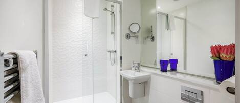 A modern bathroom with a glass-enclosed shower, a white sink, and a large mirror.