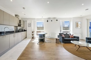A modern kitchen with a dining area, a sofa, and a glass table.
