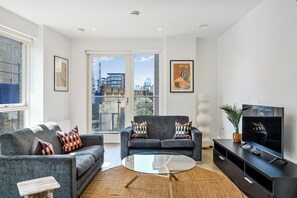 Un salon moderne comprenant un canapé, un fauteuil, une table basse en verre, un téléviseur et des œuvres d’art.