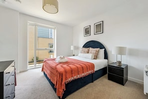 Une chambre à coucher avec un lit, deux tables de chevet, un bureau et une fenêtre.
