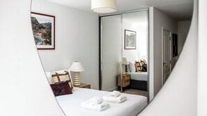 Une chambre à coucher avec un lit, une table de chevet avec une lampe, un miroir et un tableau accroché au mur.
