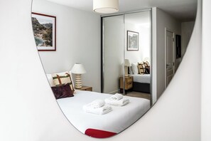 Un dormitorio con cama, una mesita de noche con lámpara, un espejo y un cuadro colgado en la pared.