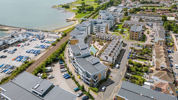 Vista aérea de una zona residencial costera con modernos edificios de apartamentos, un puerto deportivo con barcos y un amplio estacionamiento.