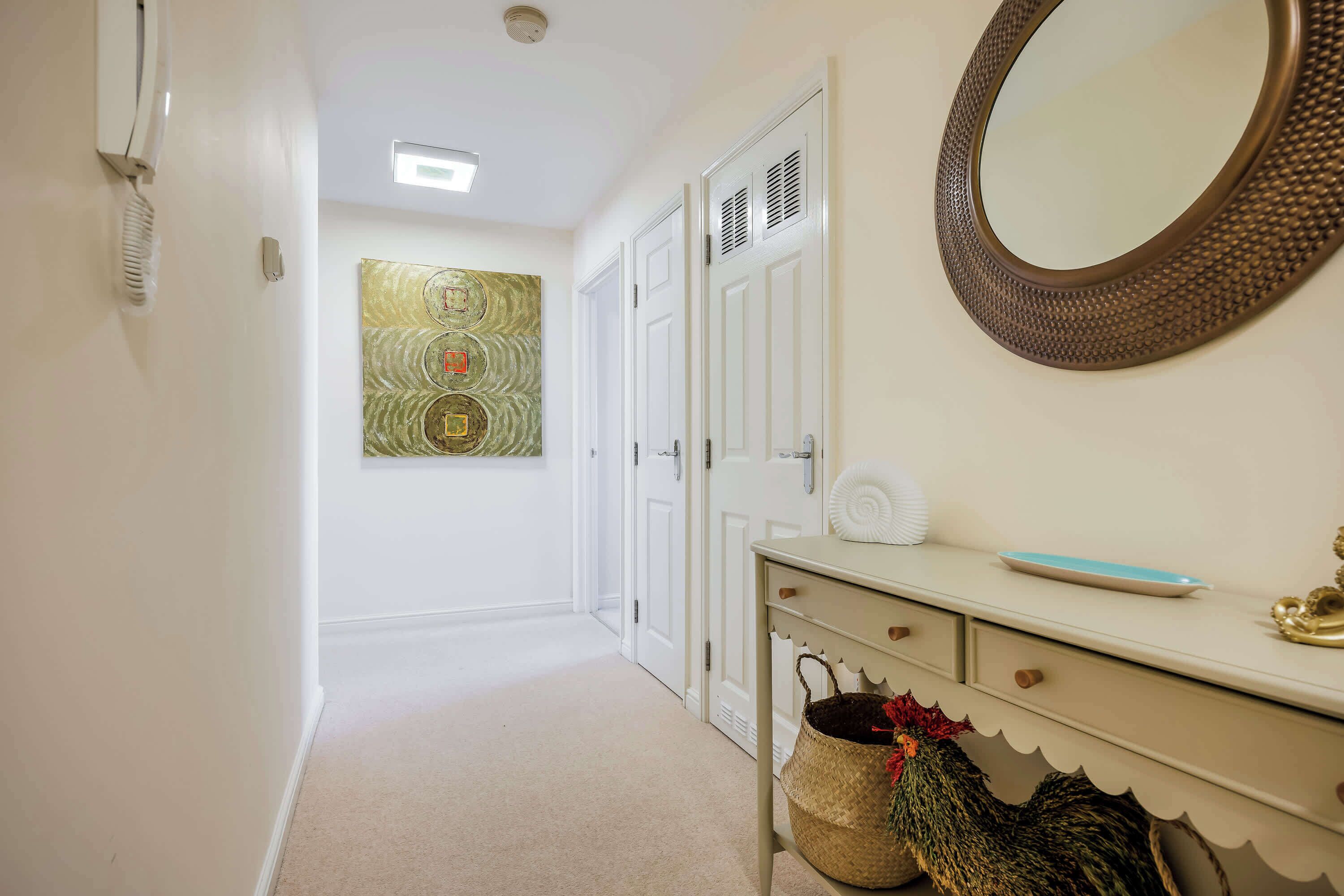 A hallway with a white door, a wall-mounted mirror, and a decorative wall piece.