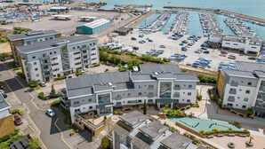 Un hotel frente al mar con varias edificaciones, un puerto deportivo con barcos y un estacionamiento.