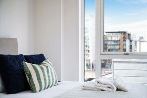 Une chambre d’hôtel avec un lit, des oreillers, une fenêtre donnant sur la ville et une serviette soigneusement pliée posée sur le lit.