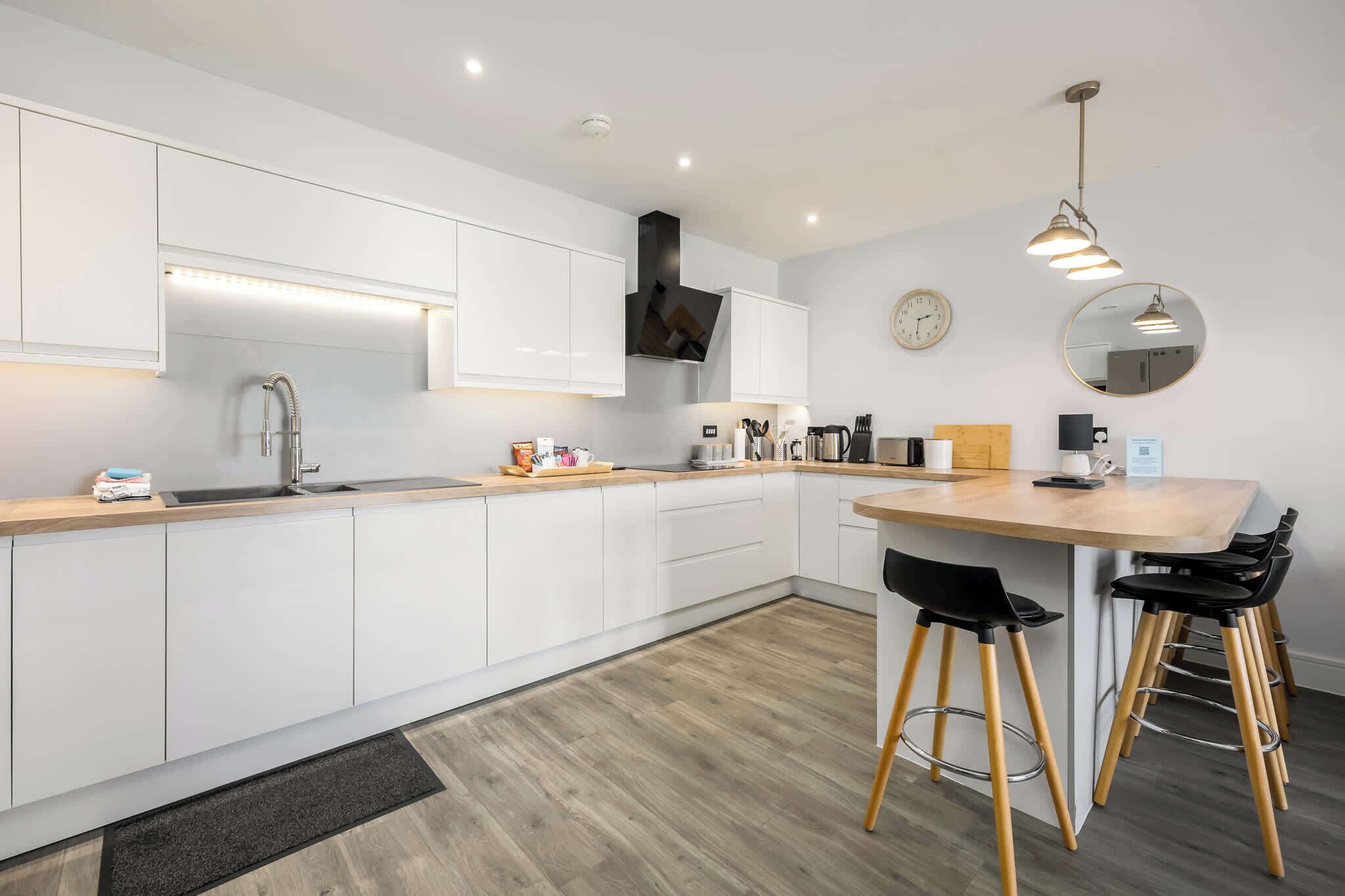 A modern kitchen with white cabinets, a wooden countertop, a sink, a stove, and a dining area with stools.