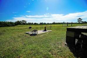 An outdoor seating area with a table and chairs, a grill, and a wooden structure.