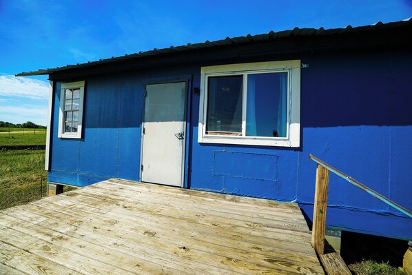A small, single-story building with a blue exterior and a wooden deck leading to a door.