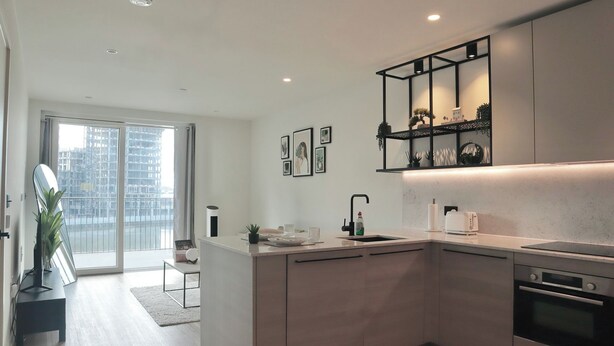 A modern kitchen with a central island, built-in oven, and a large window with a city view. - Stylish Riverside Balcony Flat Near Canary Wharf (Greater London)