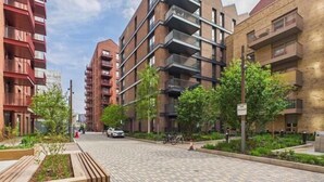 A modern urban street with multi-story residential buildings, paved sidewalks, and greenery. - Stylish Riverside Balcony Flat Near Canary Wharf (Greater London)