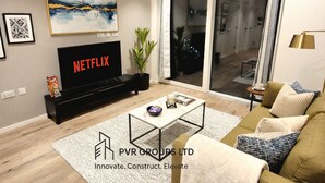 Una sala de estar con una televisión mostrando 'NETFLIX', una mesa de centro, un sofá y una planta.