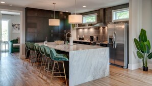 A modern kitchen with dark cabinetry, a large island with bar stools, stainless steel appliances, and pendant lighting. - Luxury 10-Bed Home w/ HUGE Rooftop & Game Room! (Nashville)