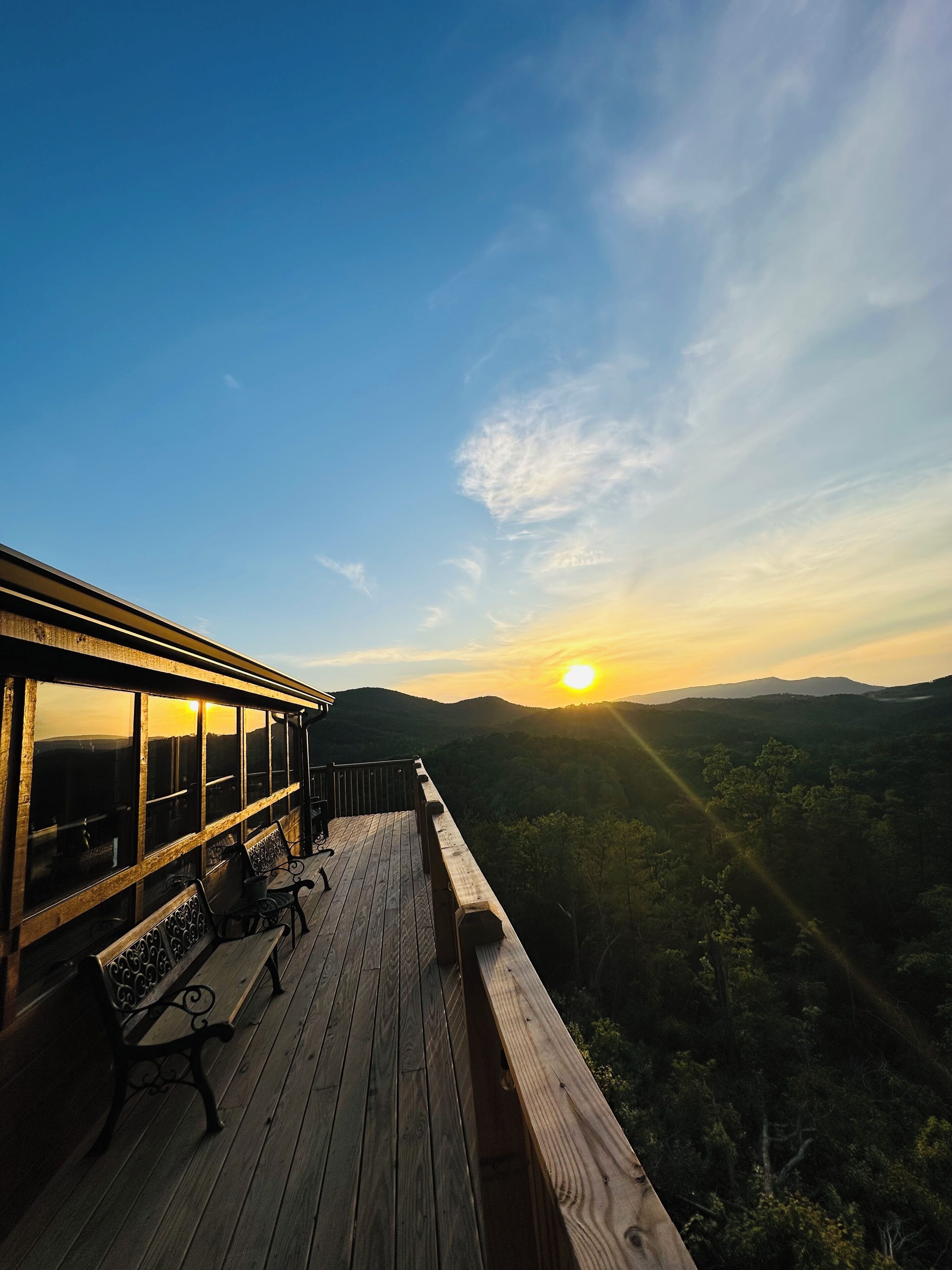 A wooden deck with a view of the sunset over a forested landscape.