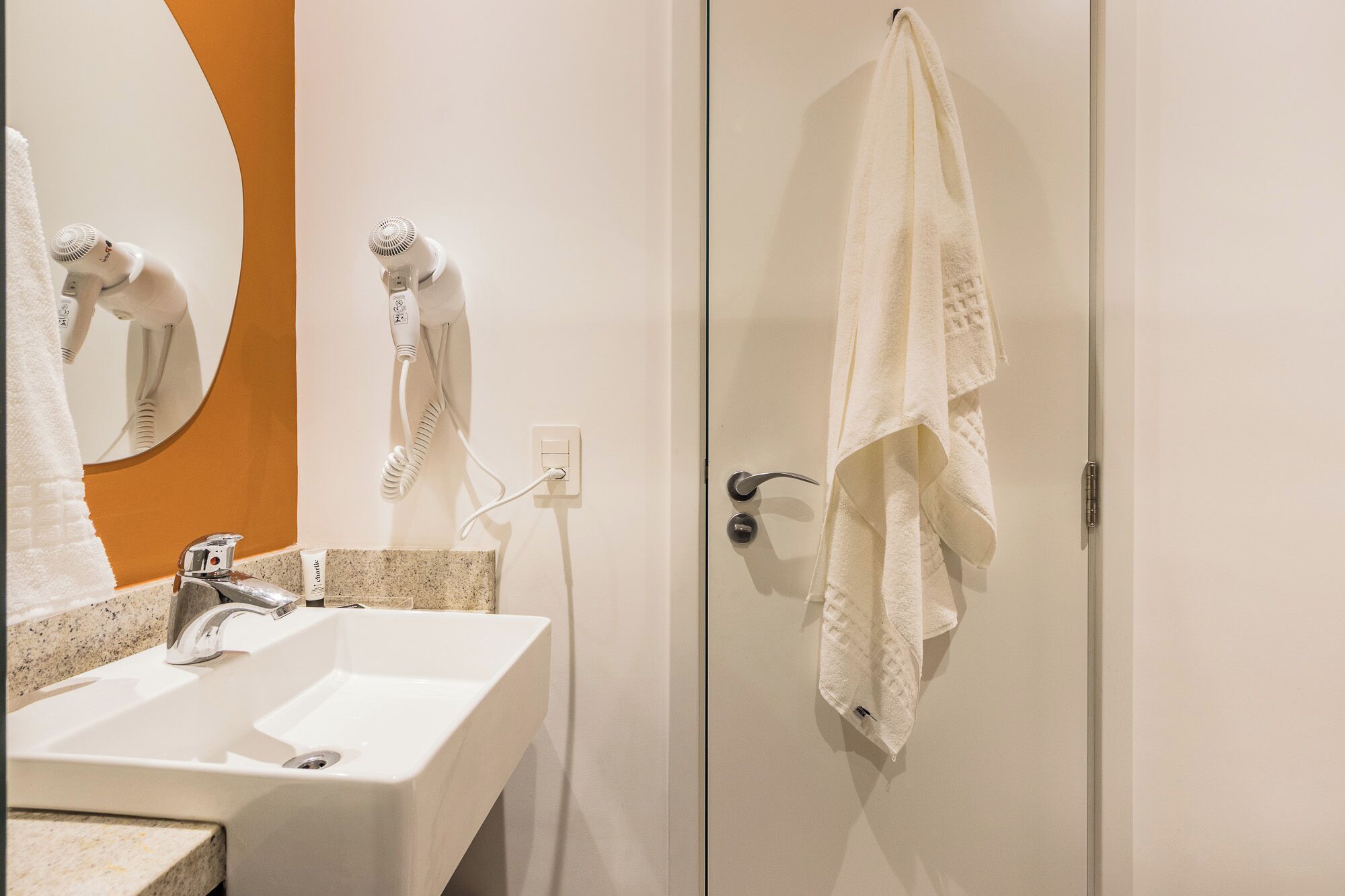 Une salle de bain avec un lavabo, un sèche-cheveux et une serviette accrochée à la porte.