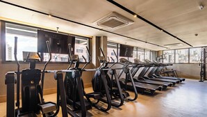 Een sportschool met loopbanden, elliptische trainers en een groot raam met uitzicht op de stad.