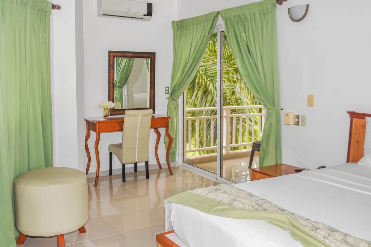 A bedroom with a bed, a desk, a chair, and a large window with curtains.