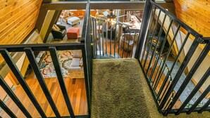 Une cabane en bois avec une chambre à coucher aménagée en mezzanine, une cheminée et une vue sur la forêt.