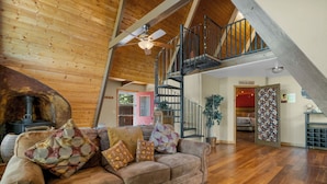 Un salon chaleureux avec un plafond en bois, un canapé agrémenté de coussins à motifs, un plancher en bois et un escalier menant à un niveau supérieur.