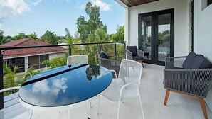 Ein Balkon mit Glastisch und weißen Stühlen, mit Blick auf ein Wohngebiet mit Bäumen und Häusern.