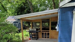 Un espacio al aire libre techado con una parrilla, un cobertizo azul y una estructura de madera.