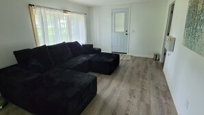 Una sala de estar con un sofá oscuro, una puerta y una pared decorada con una obra de arte texturizada.