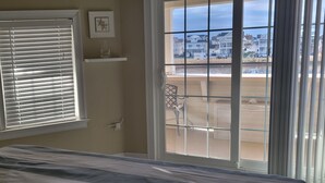 A bedroom with a bed, a window with blinds, a chair outside, and a view of a residential area.