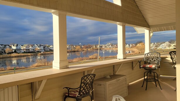 A covered porch with a view of a river and houses.