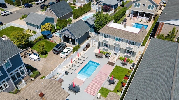 An aerial view of a residential area with a large swimming pool surrounded by outdoor seating and a covered patio area.