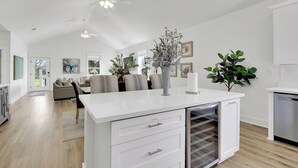 Une cuisine moderne avec des meubles blancs, un four encastré et un îlot central agrémenté d’un vase et d’une bougie.