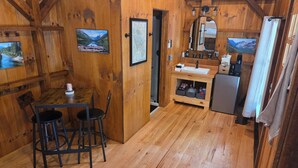 A wooden interior with a dining table, chairs, a refrigerator, a sink, and framed pictures on the walls. - Lazy T Cabins - Glacier (Graham County)