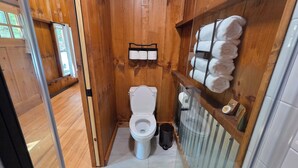 A compact wooden bathroom with a toilet, a towel rack, and a glass shower enclosure. - Lazy T Cabins - Glacier (Graham County)
