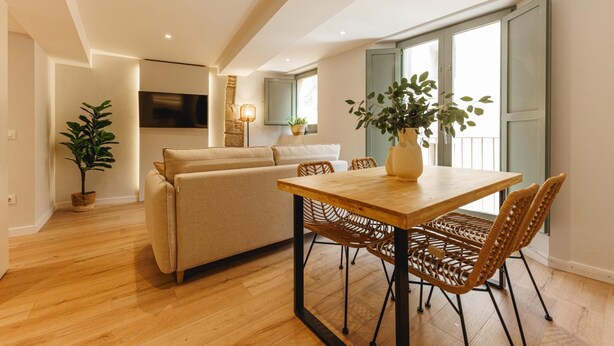Un salon moderne avec une table à manger en bois, des chaises en osier, un canapé beige et une plante en pot.