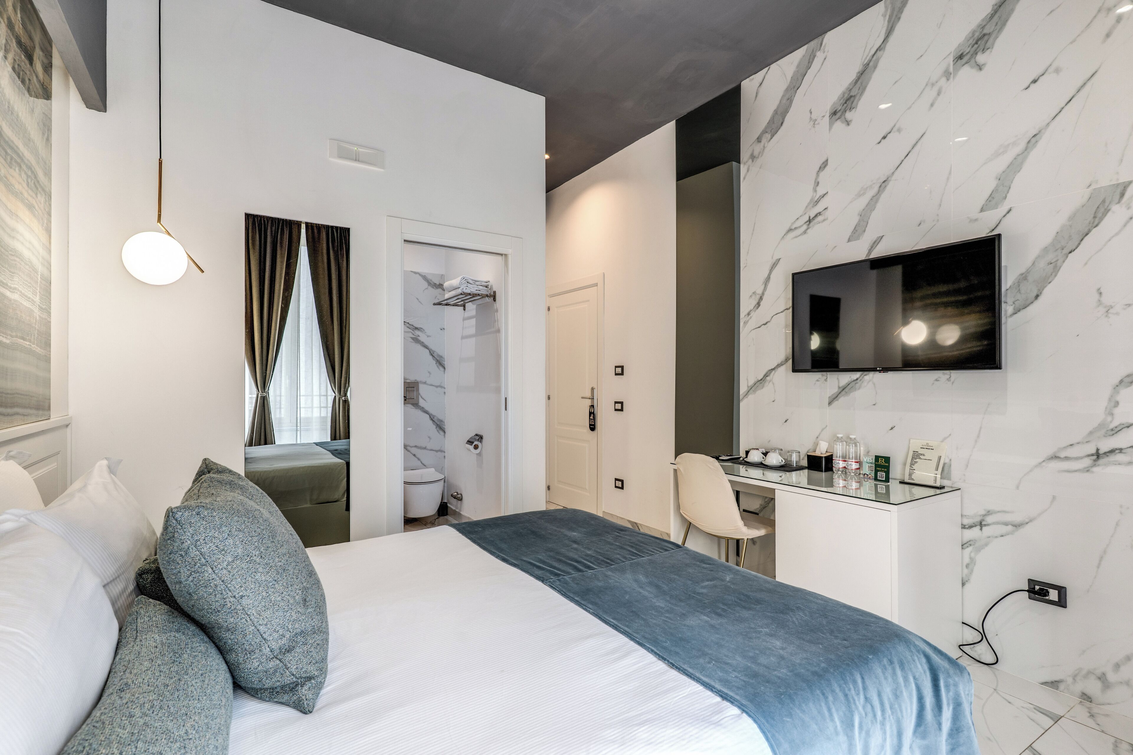 A modern hotel room with a bed, a desk, a chair, a TV, and a bathroom.