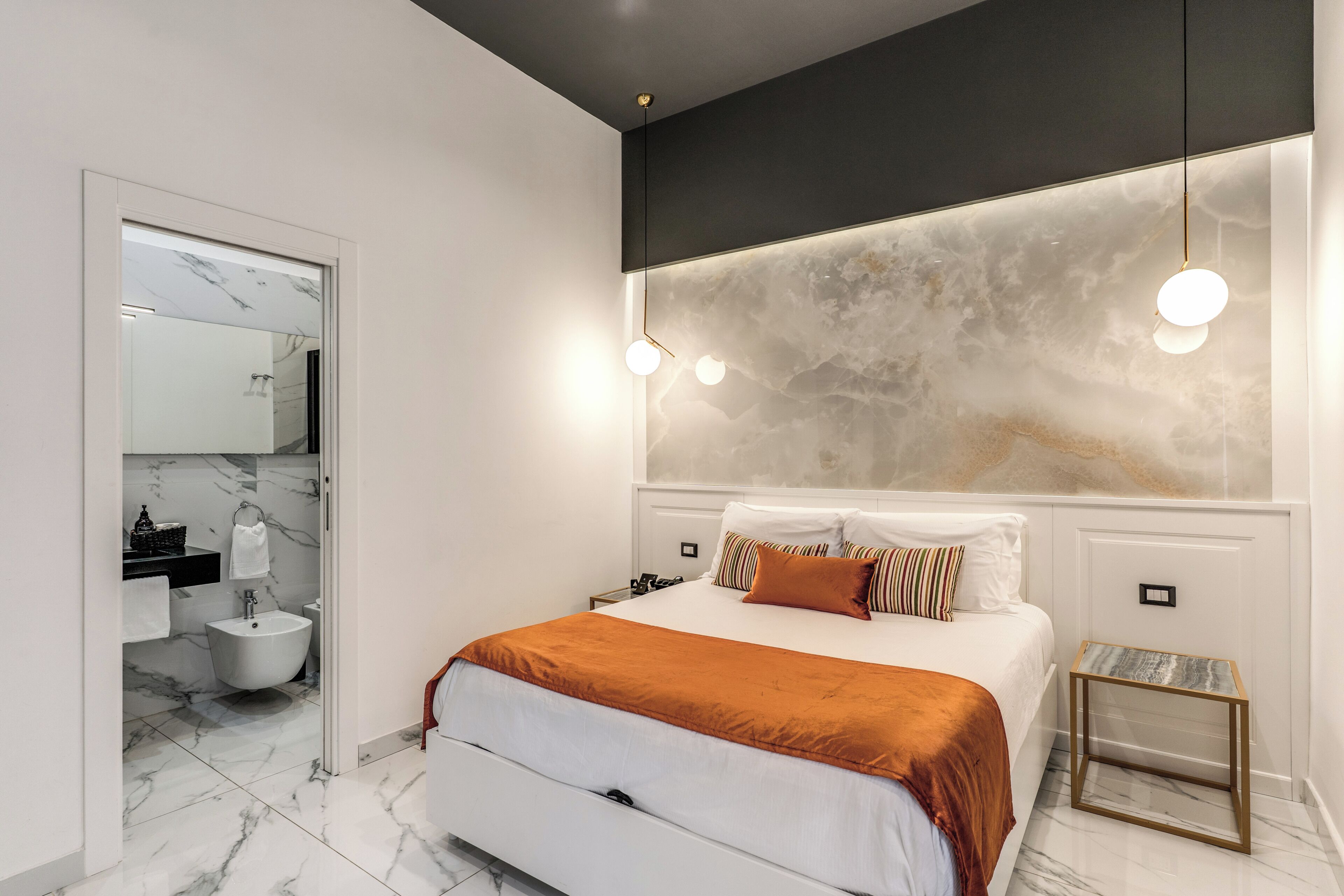 A modern bedroom with a bed, bedside tables, a nightstand, and a bathroom with a sink and mirror.