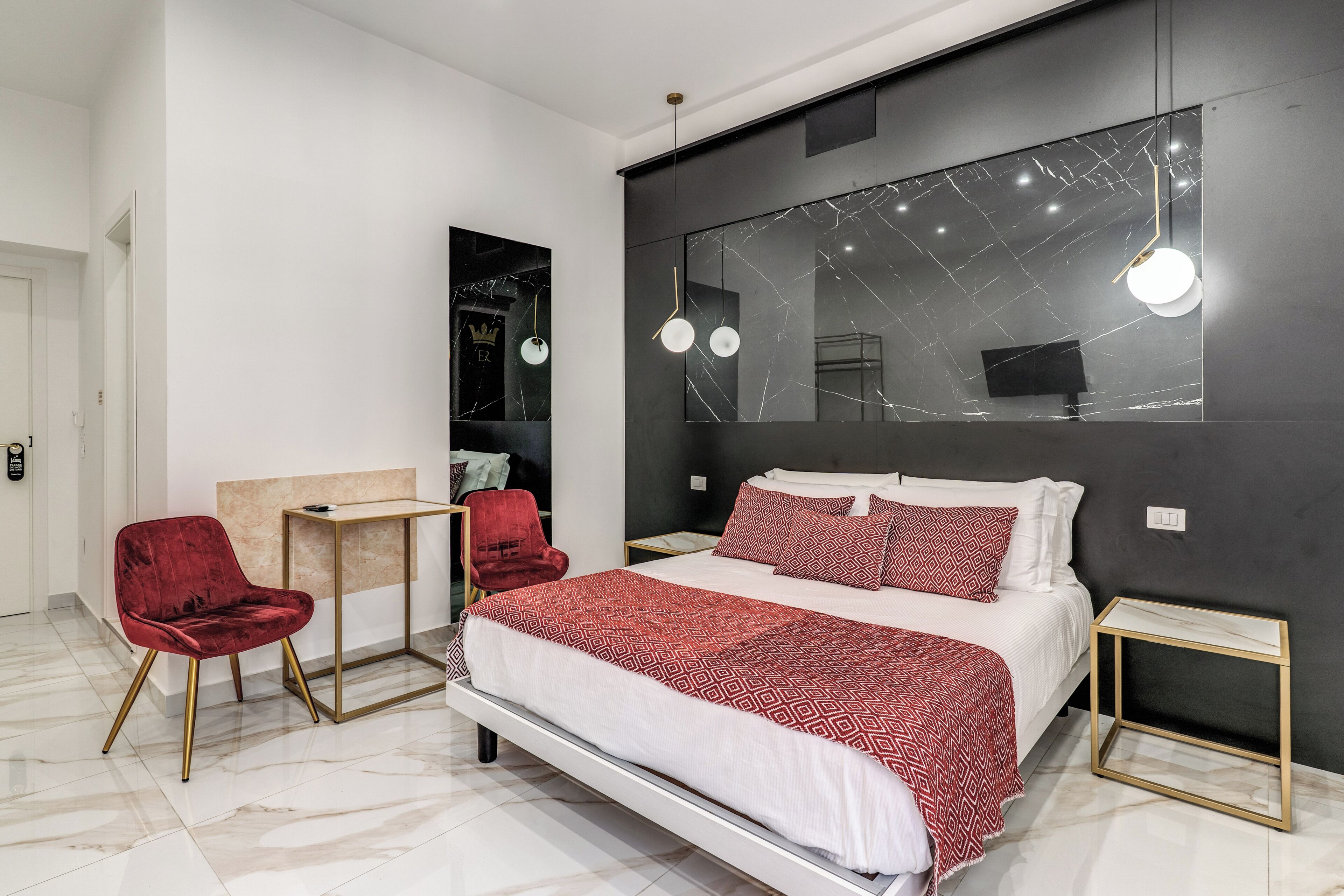 A modern bedroom with a bed, a red chair, a small table, and a mirror on the wall.