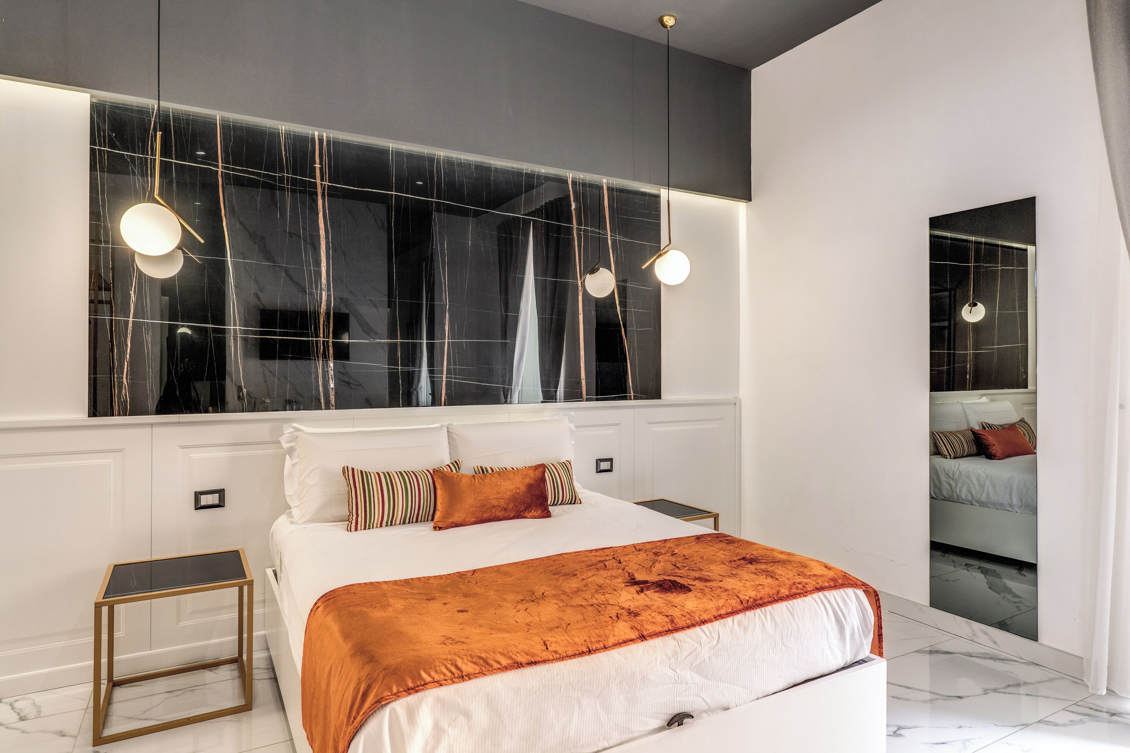 A modern bedroom with a large bed, bedside tables, a mirror, and a view of another room.