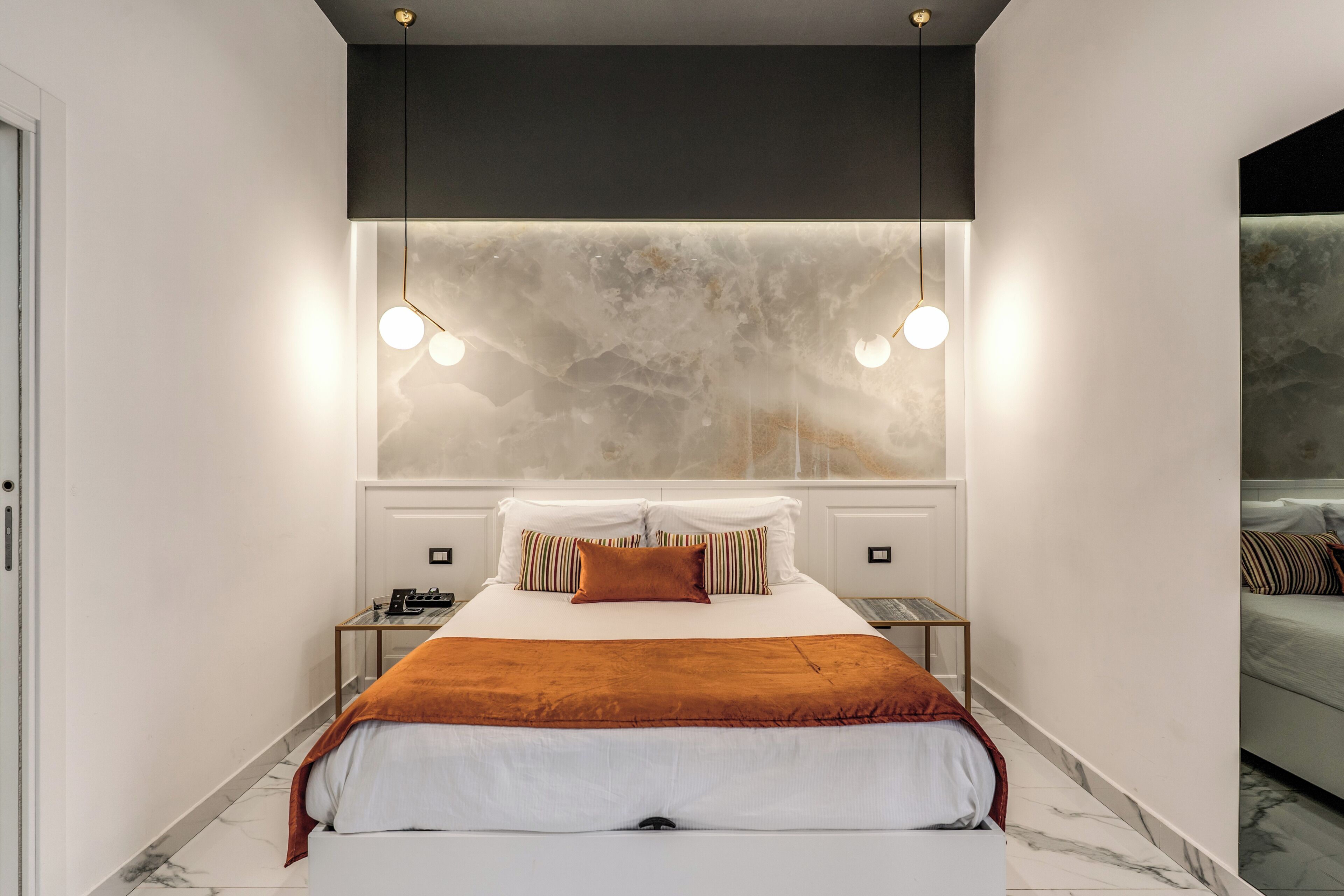 A modern bedroom with a large bed, bedside tables, and a marble wall.