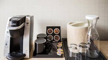 Une machine à café, des dosettes de café, des tasses, un moulin et une bouteille d’eau, le tout sur un plateau.