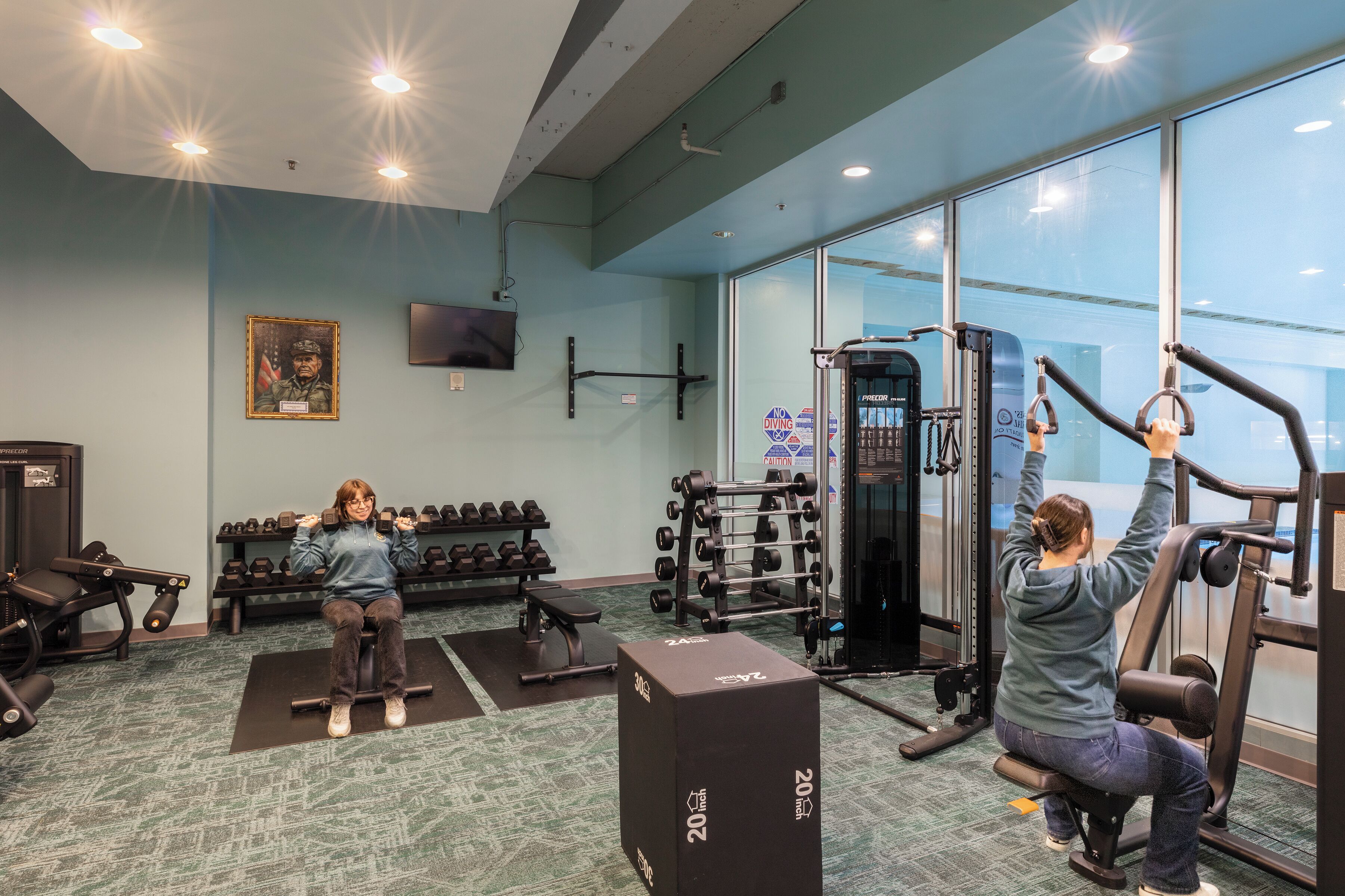 A gym with exercise equipment, dumbbells, and a television on the wall.