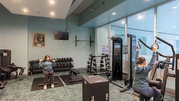 A gym with exercise equipment, dumbbells, and a television on the wall.