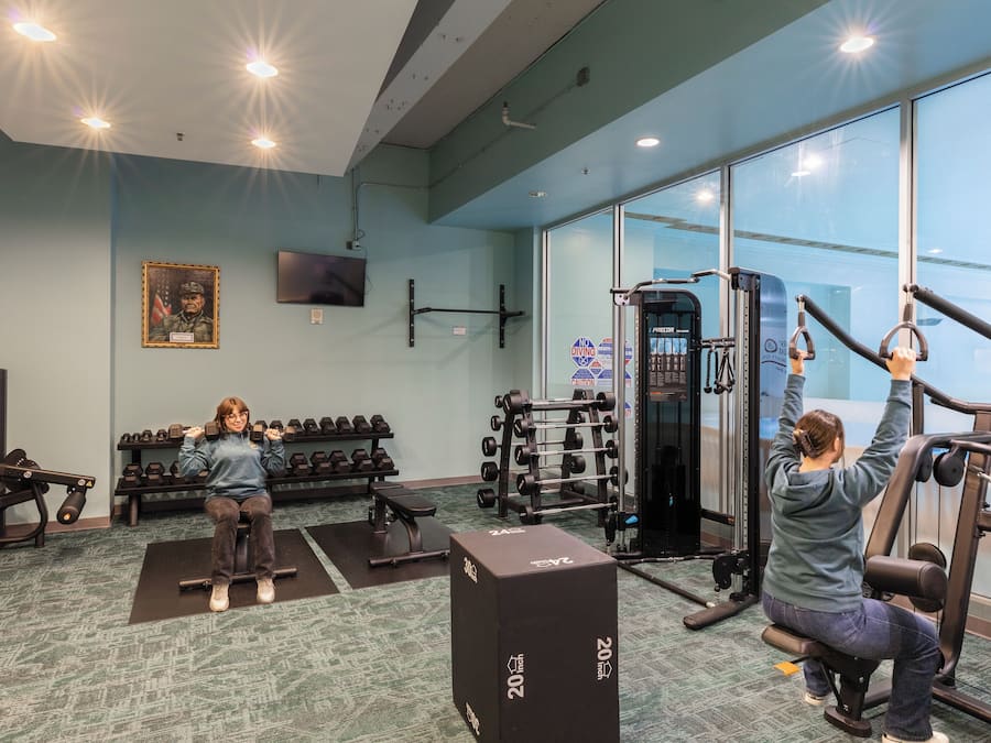 A gym with exercise equipment, dumbbells, and a television on the wall.