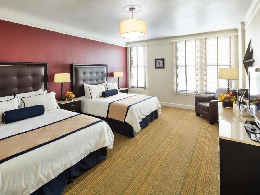 A hotel room with two beds, a desk, and a TV.