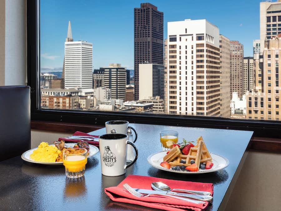 A breakfast table with a city view, a coffee mug, and plates of food.