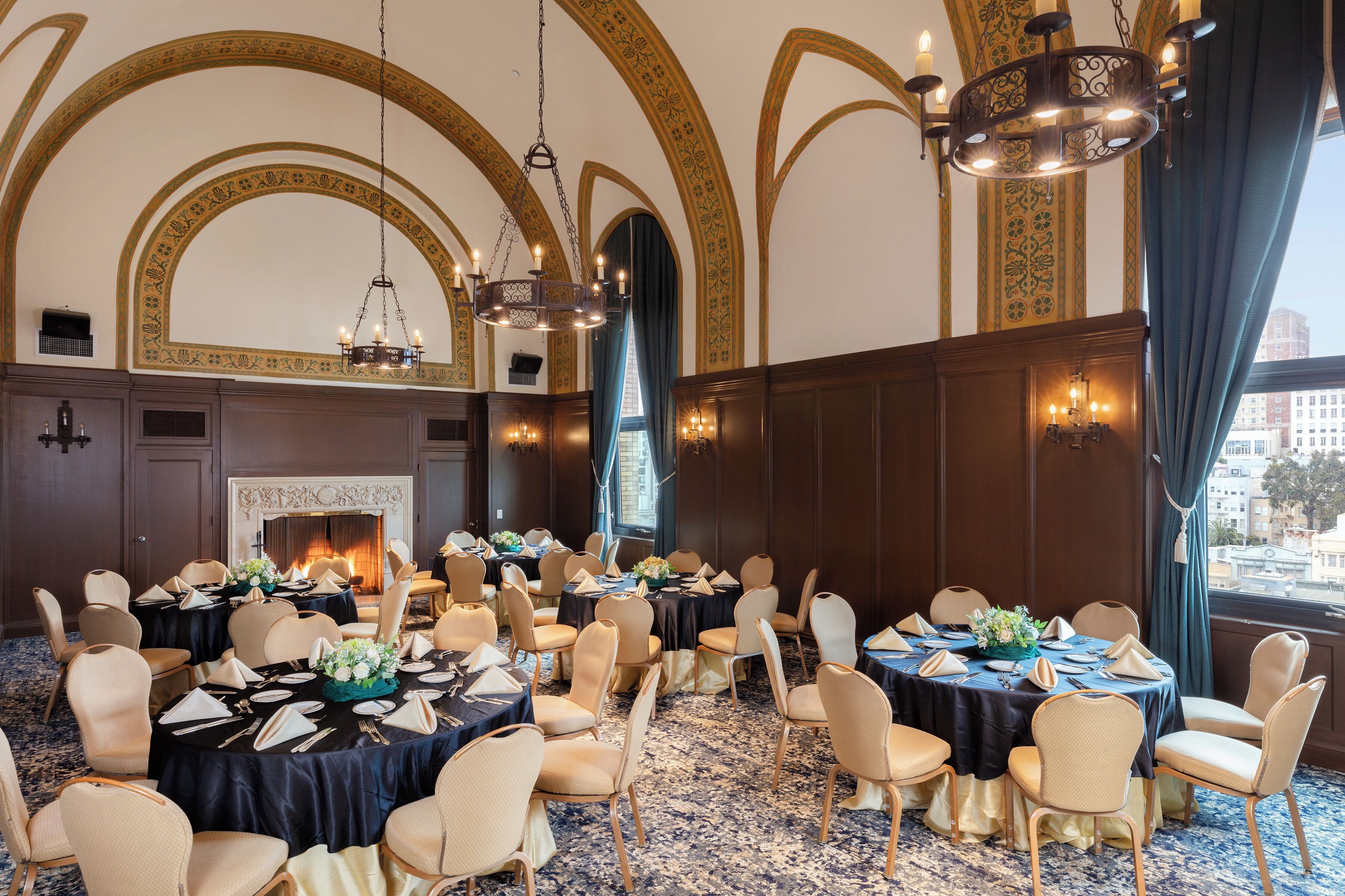 A banquet hall with round tables, chairs, chandeliers, and a fireplace.