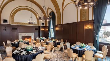 A banquet hall with round tables, chairs, chandeliers, and a fireplace.