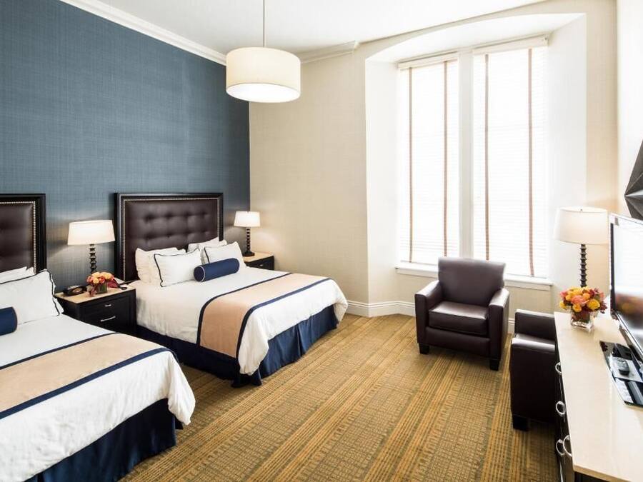 A hotel room with two beds, a desk, a chair, and a large window.