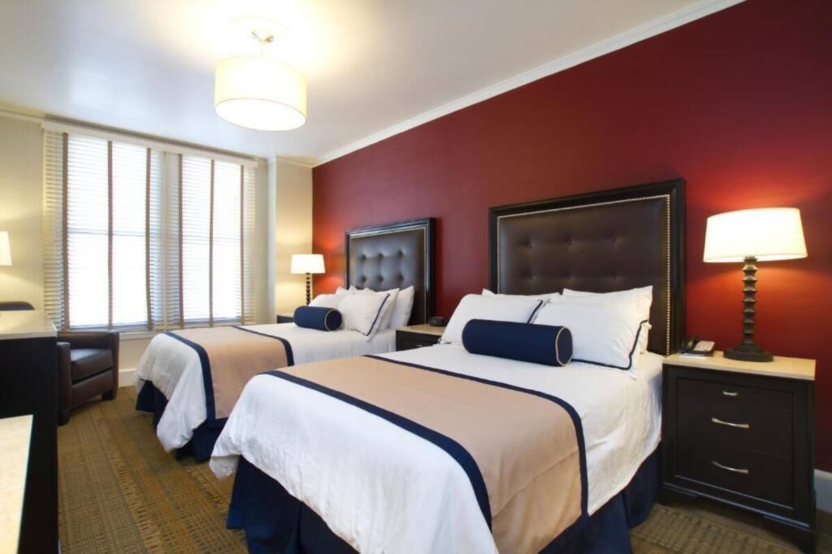 Quarto de hotel com duas camas, uma escrivaninha e uma mesa de cabeceira com luminárias.