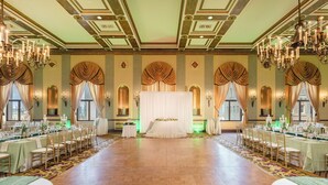A banquet hall with a central stage, chandeliers, and rows of tables set for a formal event. - Marines Memorial Club & Hotel  (San Francisco)