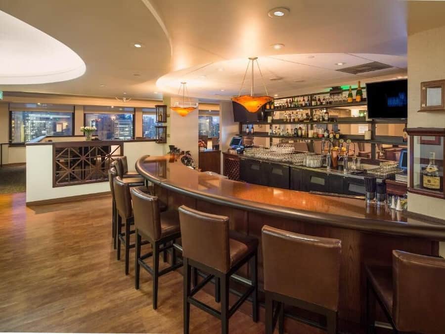 Un espace bar doté d’un comptoir incurvé, de tabourets de bar et offrant une vue sur la ville grâce à de grandes fenêtres.